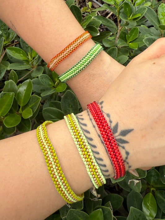Wrist with colorful beaded bracelets against a green leafy background