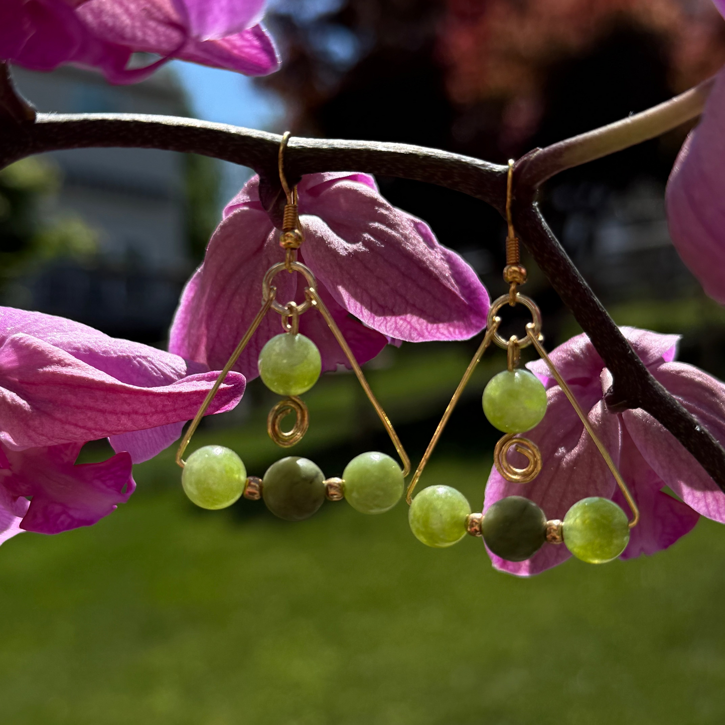 Green beaded earrings hanging on a branch with pink flowers