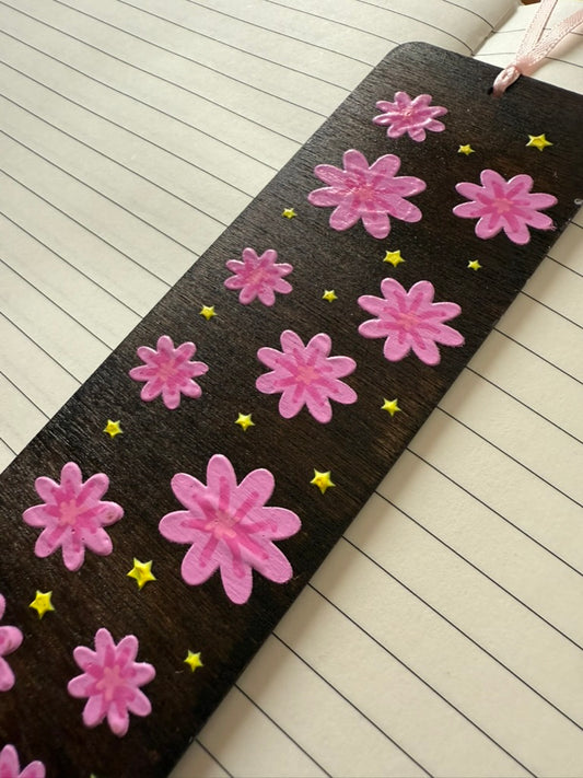 Floral-patterned bookmark with pink flowers and yellow stars on a wooden floor.