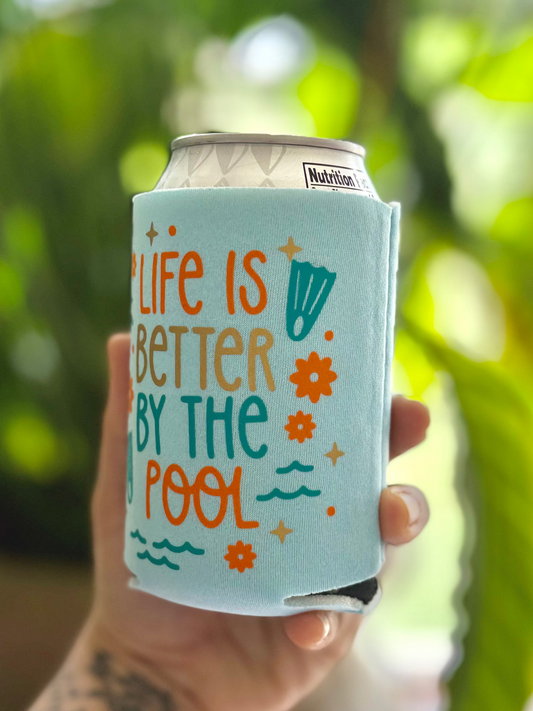 Can cooler with 'Life is better by the pool' text held in a hand against a blurred green background