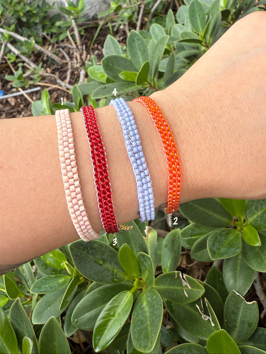 Wrist wearing multiple beaded bracelets with a green leafy background