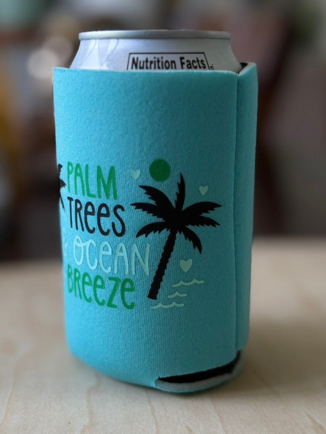 Teal can cooler with palm tree and ocean text design on a wooden surface