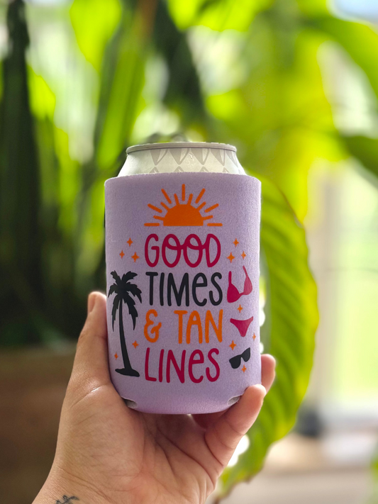 Hand holding a can with 'Good Times & Tan Lines' design against a blurred green background