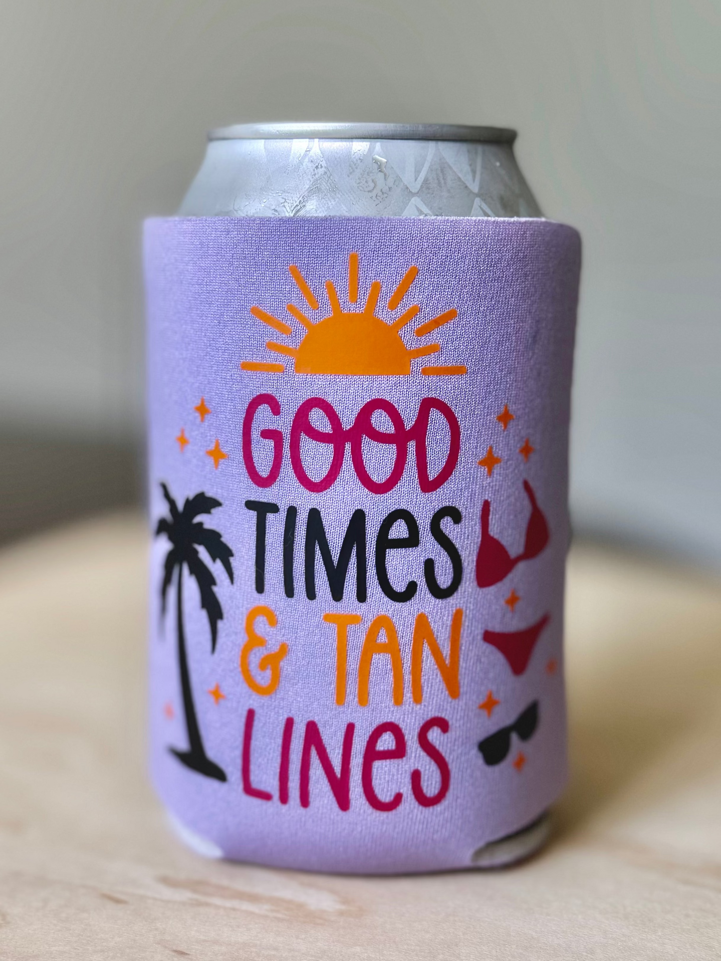 Purple can cooler with 'Good Times & Tan Lines' text on a wooden surface