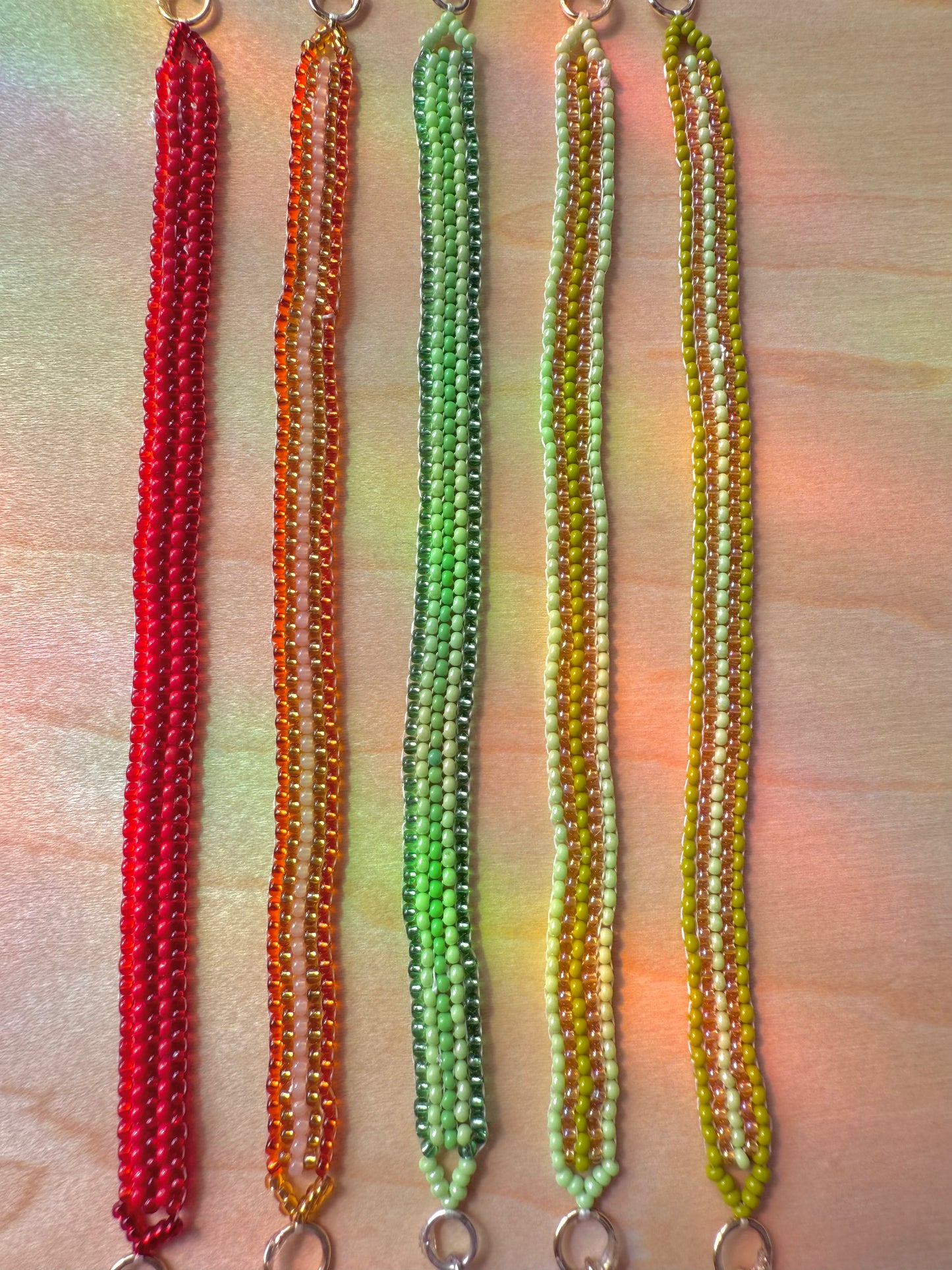Five beaded necklaces in red, orange, green, and yellow on a wooden surface.