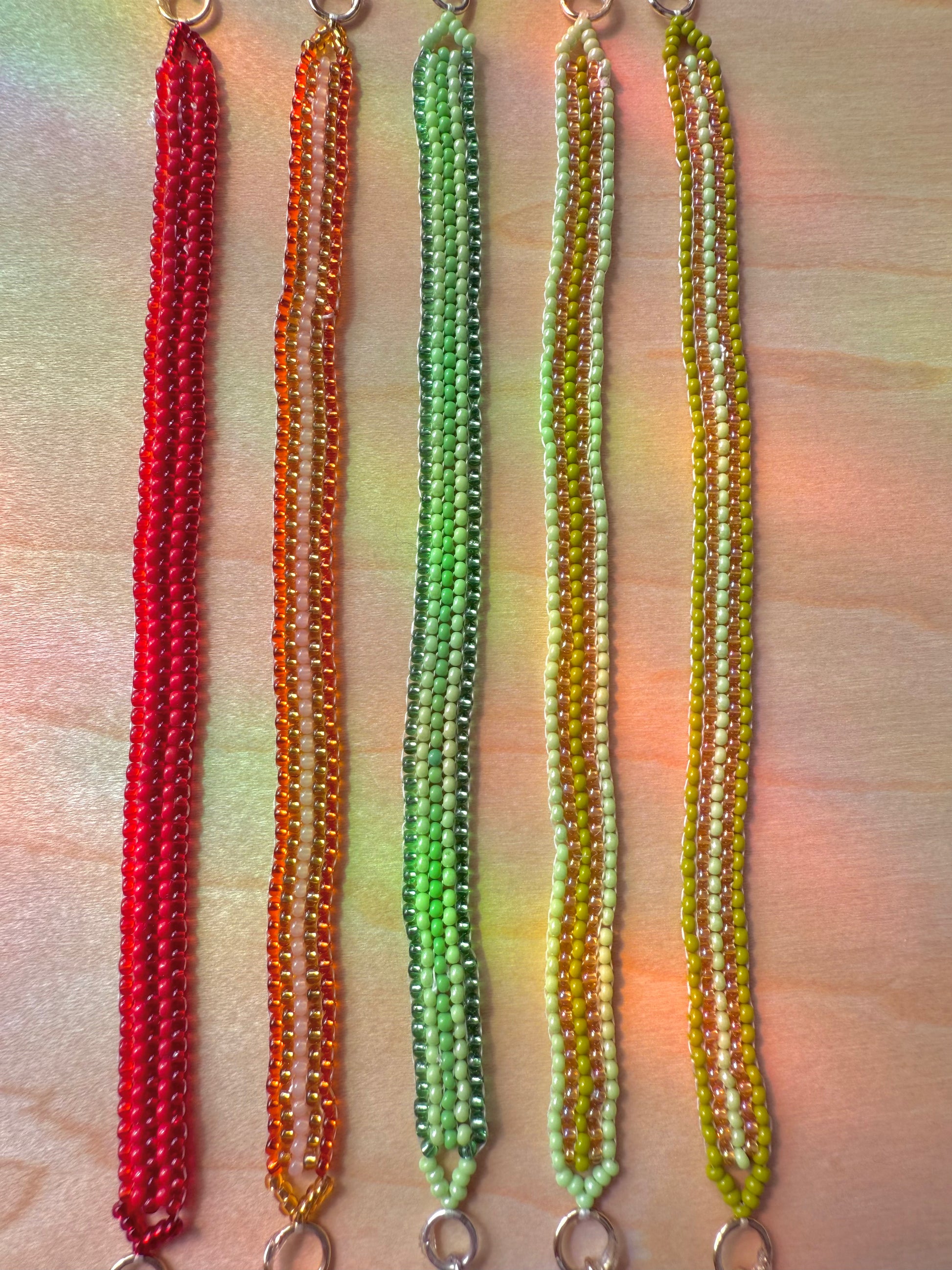 Five beaded necklaces in red, orange, green, and yellow on a wooden surface.