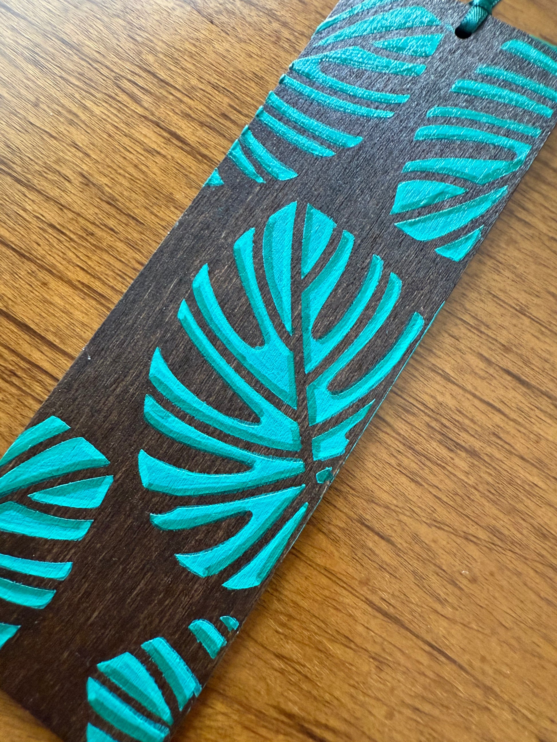 Wooden bookmark with teal leaf pattern on a wooden surface