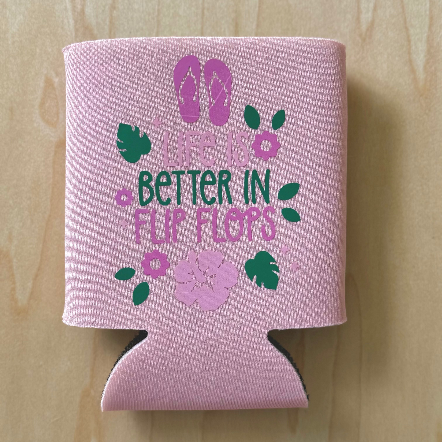 Pink can cooler with flip flop design and text on a wooden surface