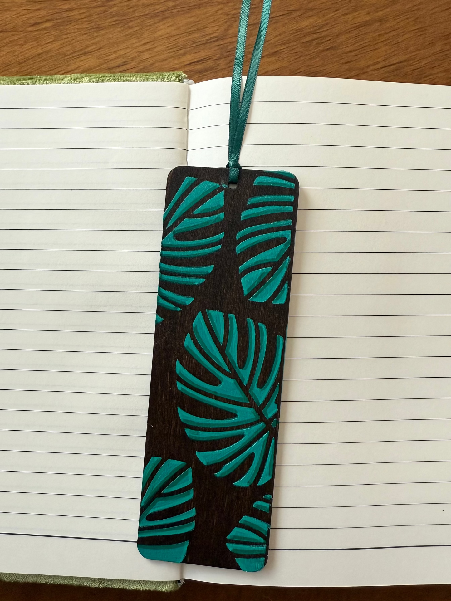Bookmark with green leaf pattern on black background, placed on an open notebook.