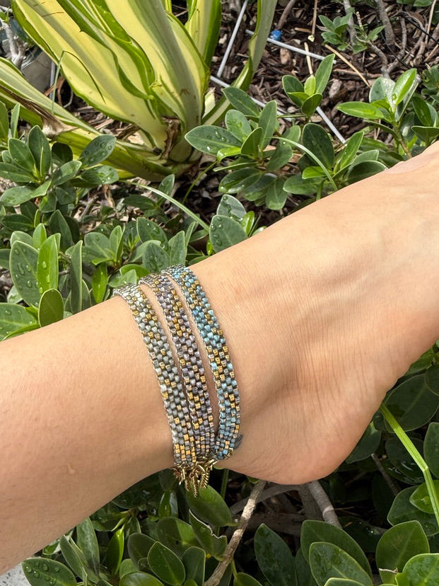 Close-up of a wrist wearing a beaded bracelet with greenery in the background