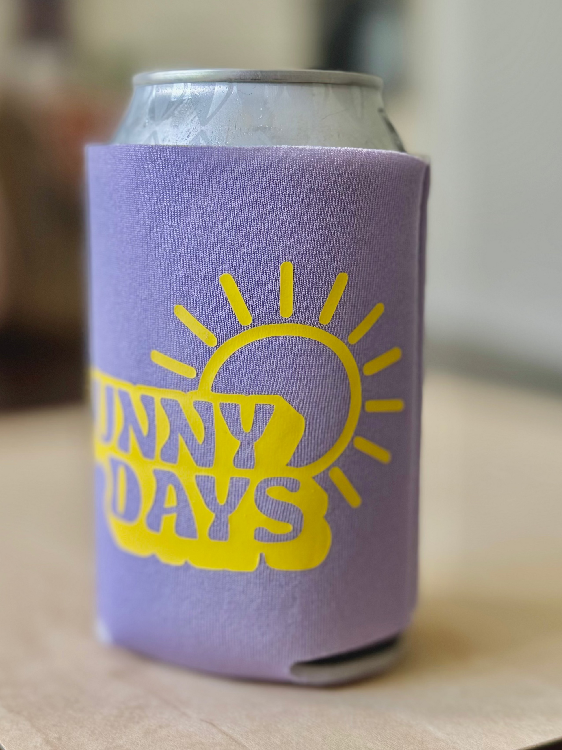 Can with a purple sleeve featuring a yellow sun graphic and 'Sunny Days' text on a wooden surface.
