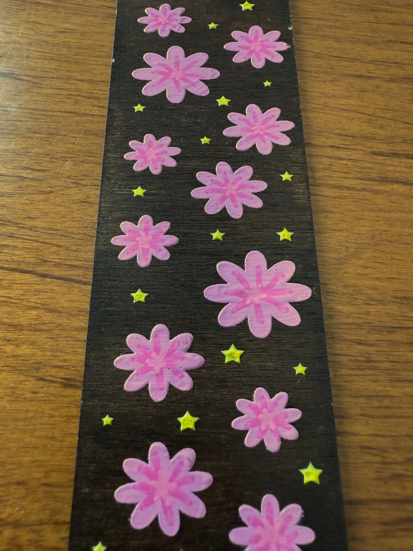 Pink flowers on a black bookmark with yellow stars on a wooden surface