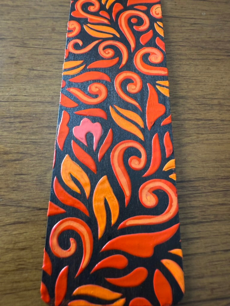 Decorative bookmark with orange and red floral pattern on a wooden surface