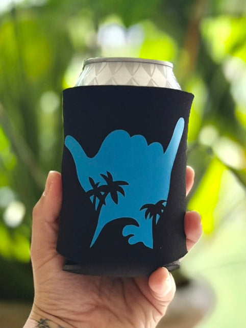 Hand holding a can with a blue design against a blurred green leafy background