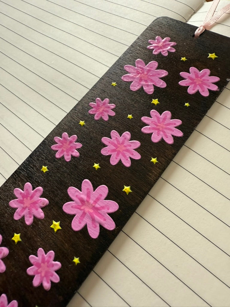 Floral-patterned bookmark with pink flowers and yellow stars on a wooden floor.