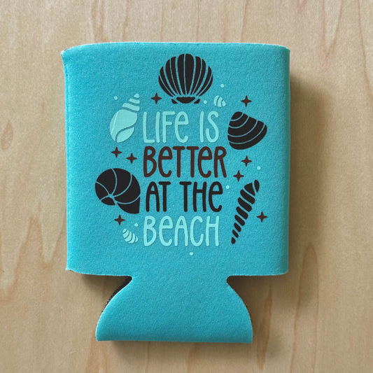 Turquoise can cooler with 'Life is Better at the Beach' text and shell graphics on a wooden surface