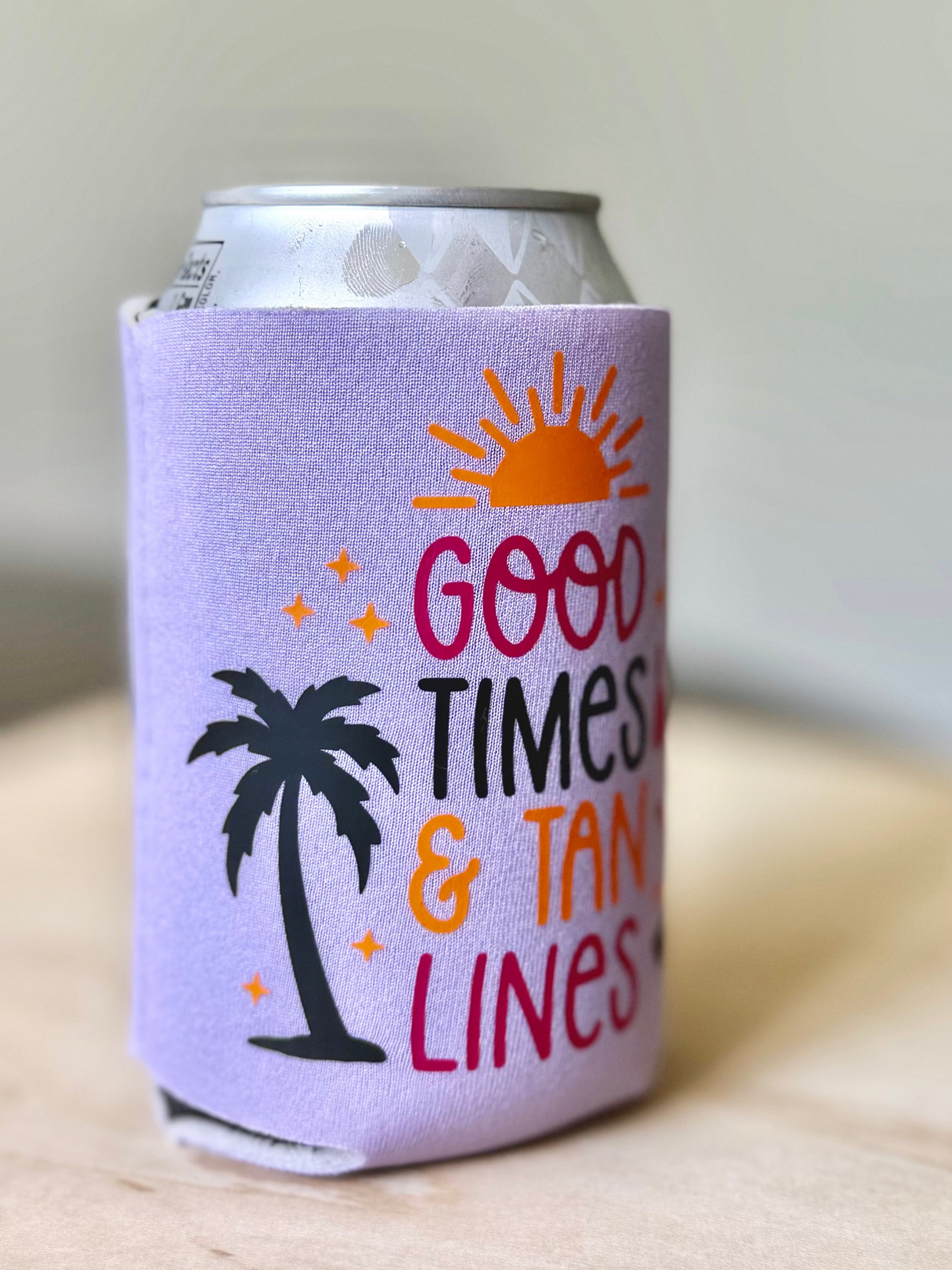 Can cooler with 'Good Times & Tan Lines' text and palm tree design on a wooden surface.