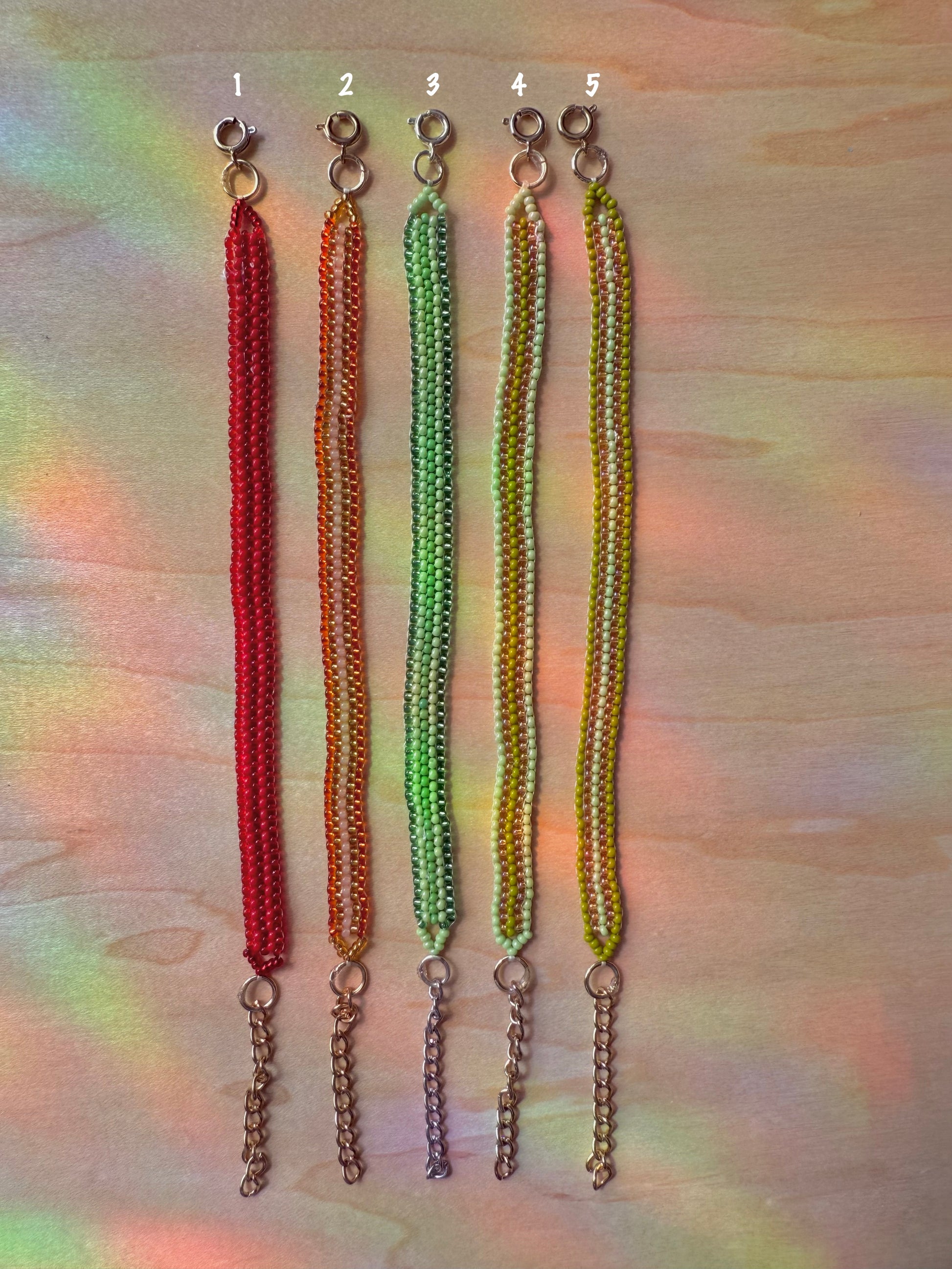 Five beaded keychains in red, orange, green, and yellow on a multicolored background.