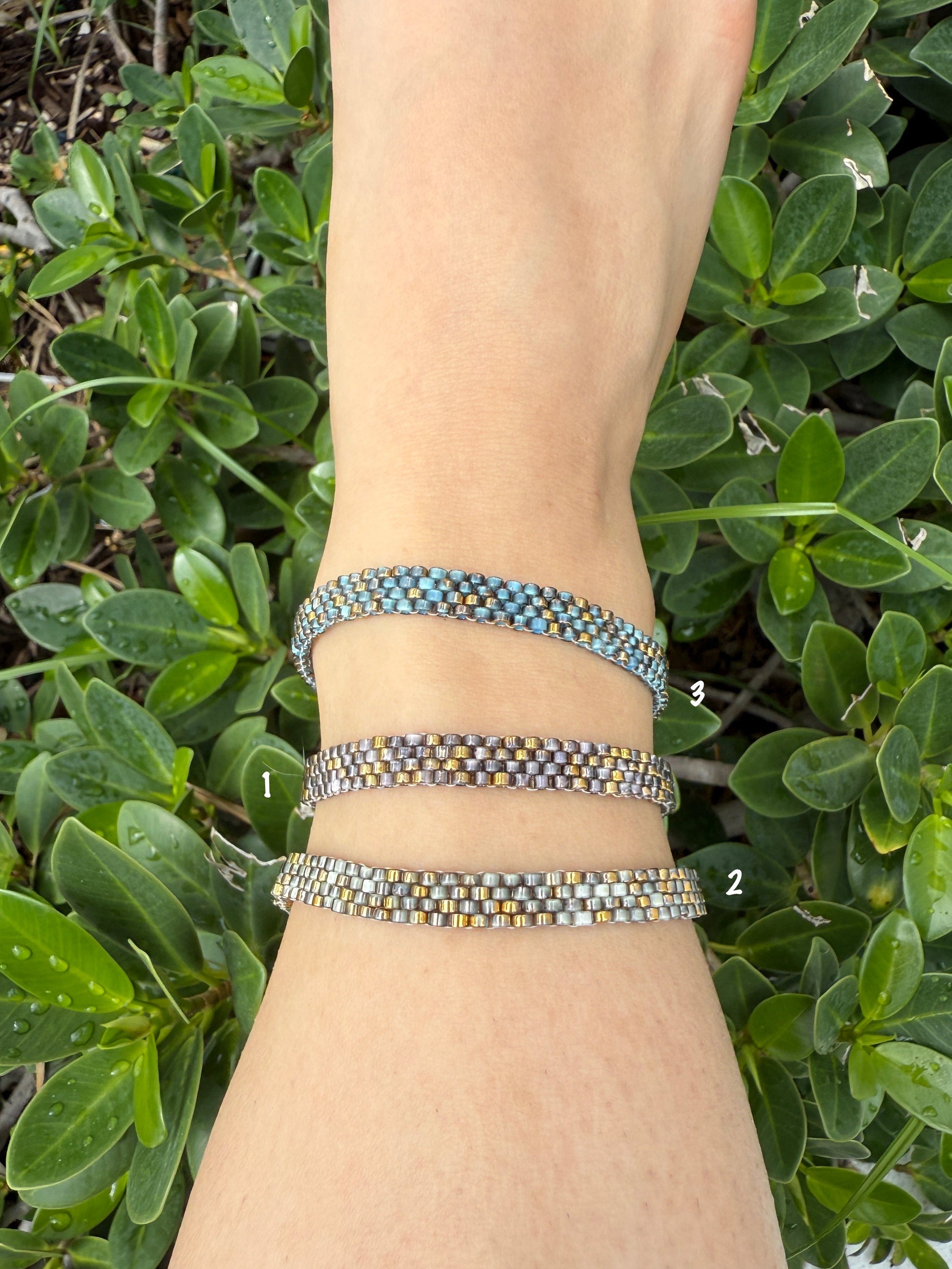 Wrist with multiple bracelets against a green leafy background