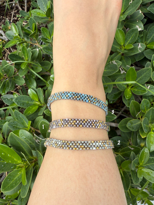 Wrist with multiple bracelets against a green leafy background