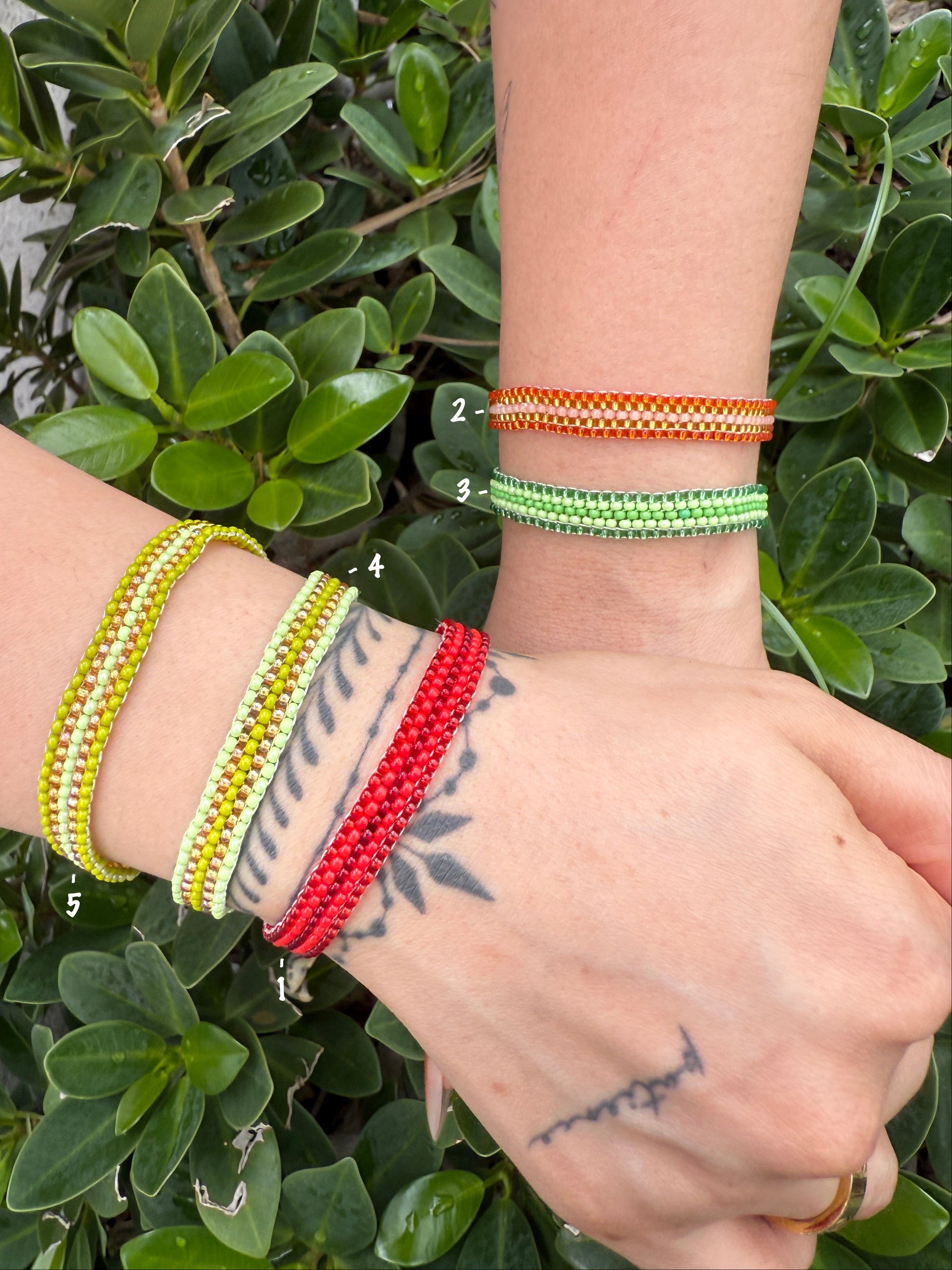 Close-up of a wrist wearing multiple colorful beaded bracelets against a green leafy background