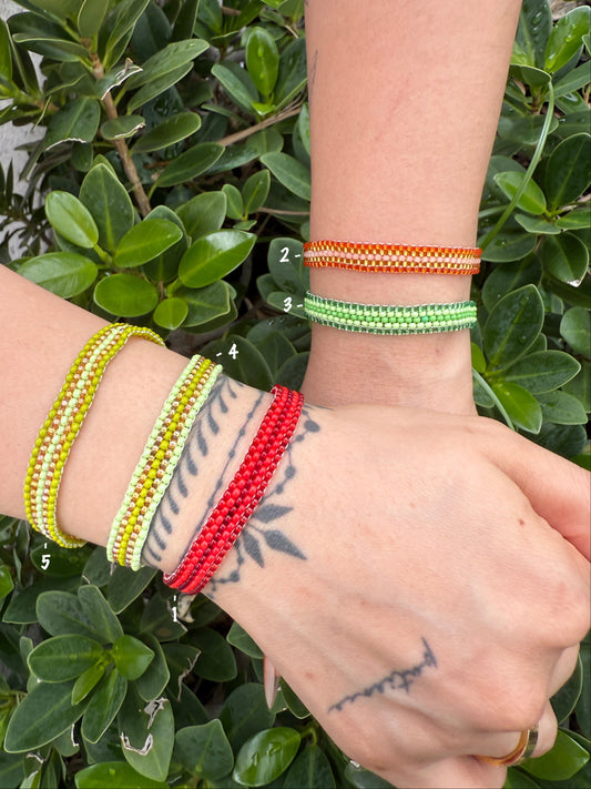 Close-up of a wrist wearing multiple colorful beaded bracelets against a green leafy background