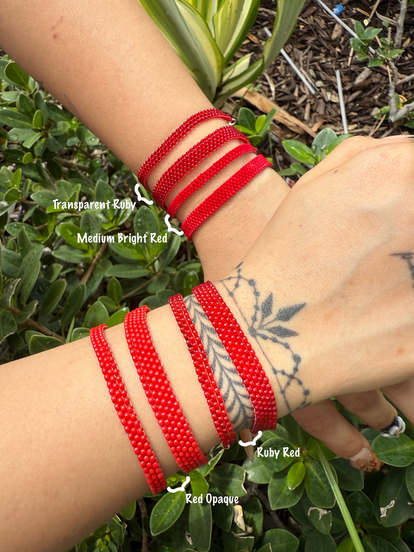 Red beaded bracelets on a wrist with green foliage background