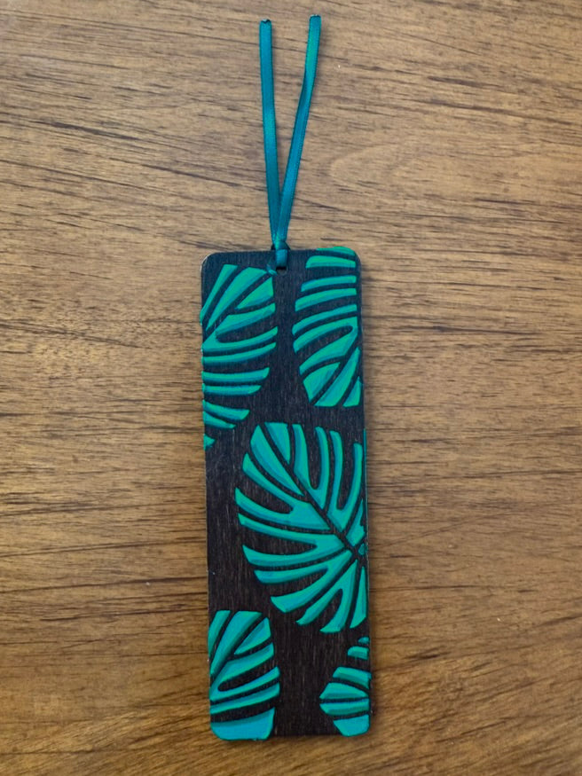 Bookmark with teal leaf pattern on black background on a wooden surface