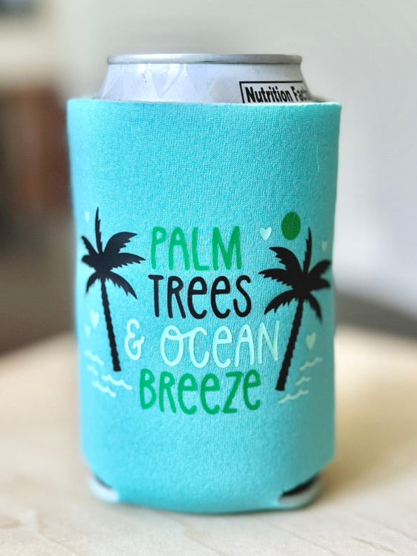 Light blue can cooler with palm tree and ocean breeze design on a wooden surface.