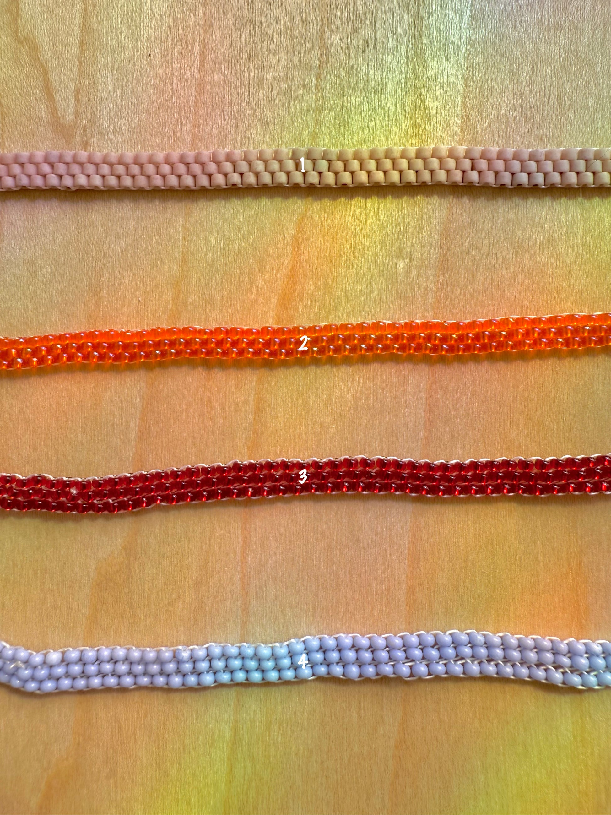 Four colorful beaded strings on a textured fabric background