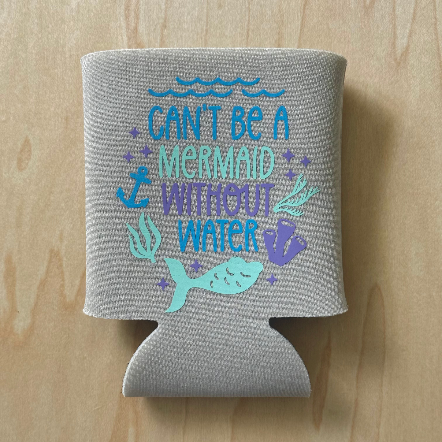 Gray can cooler with mermaid-themed design on a wooden surface