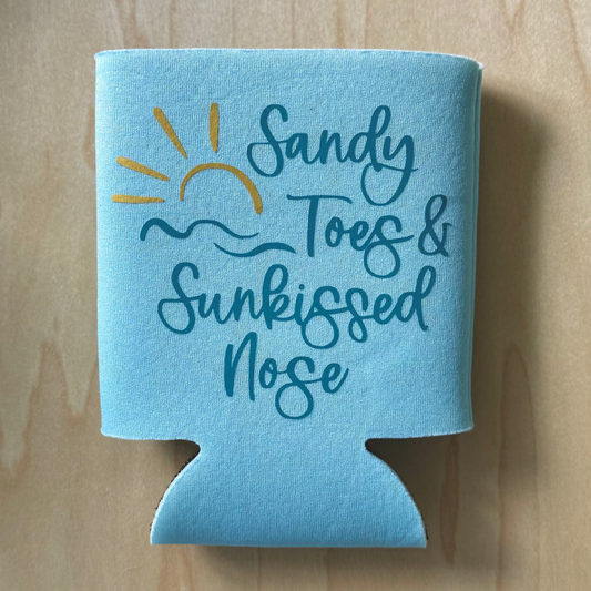 Blue can cooler with 'Sandy Toes & Sunkissed Nose' text on a wooden surface