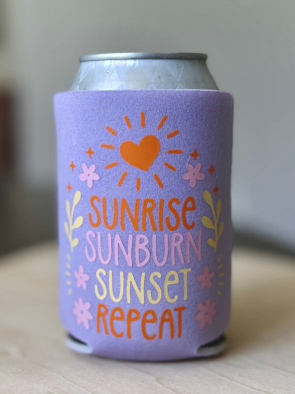 Purple can cooler with 'Sunrise Sunburn Sunset Repeat' text on a wooden surface.