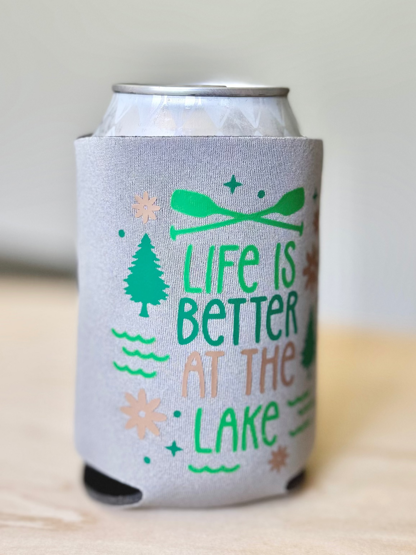 Gray can cooler with 'Life is Better at the Lake' text and nature-themed graphics on a light wooden surface.