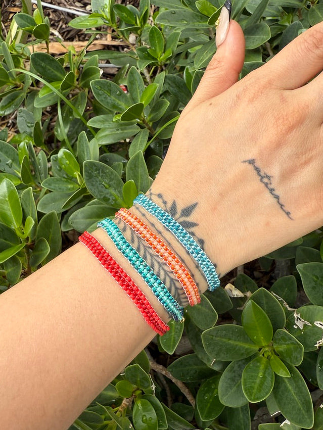 Hand wearing colorful bracelets with a green leafy background