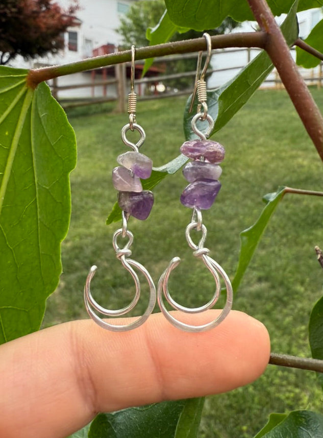 Silver earrings with purple stones held between green leaves