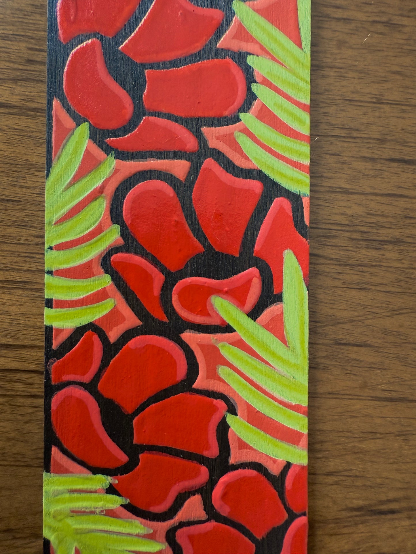 Decorative bookmark with red floral pattern and green leaves on a wooden surface