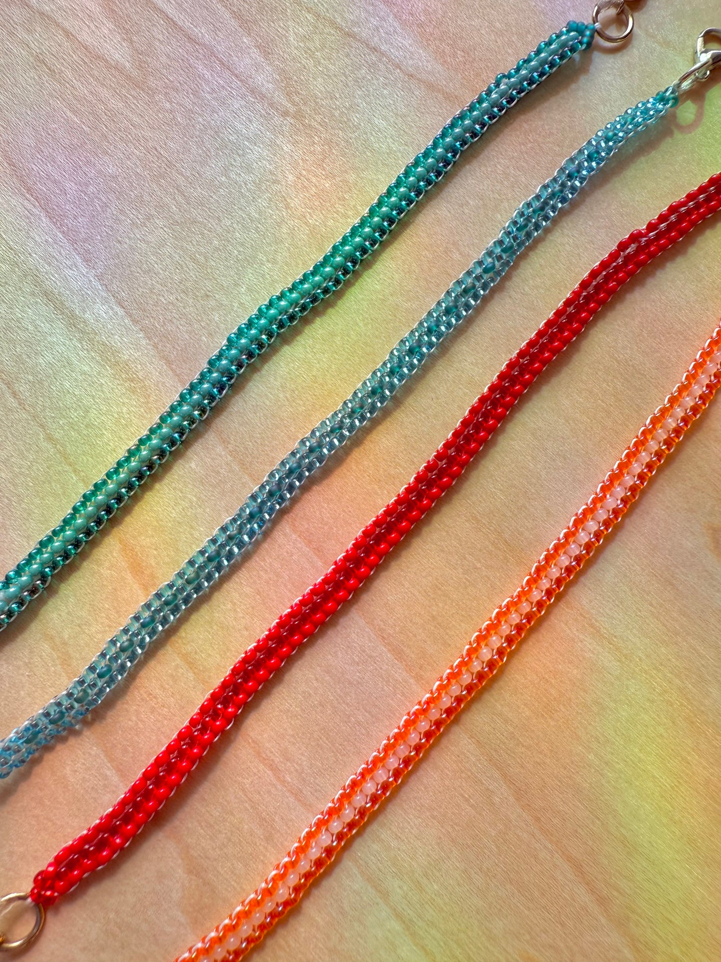 Three beaded necklaces in turquoise, red, and orange on a textured surface.