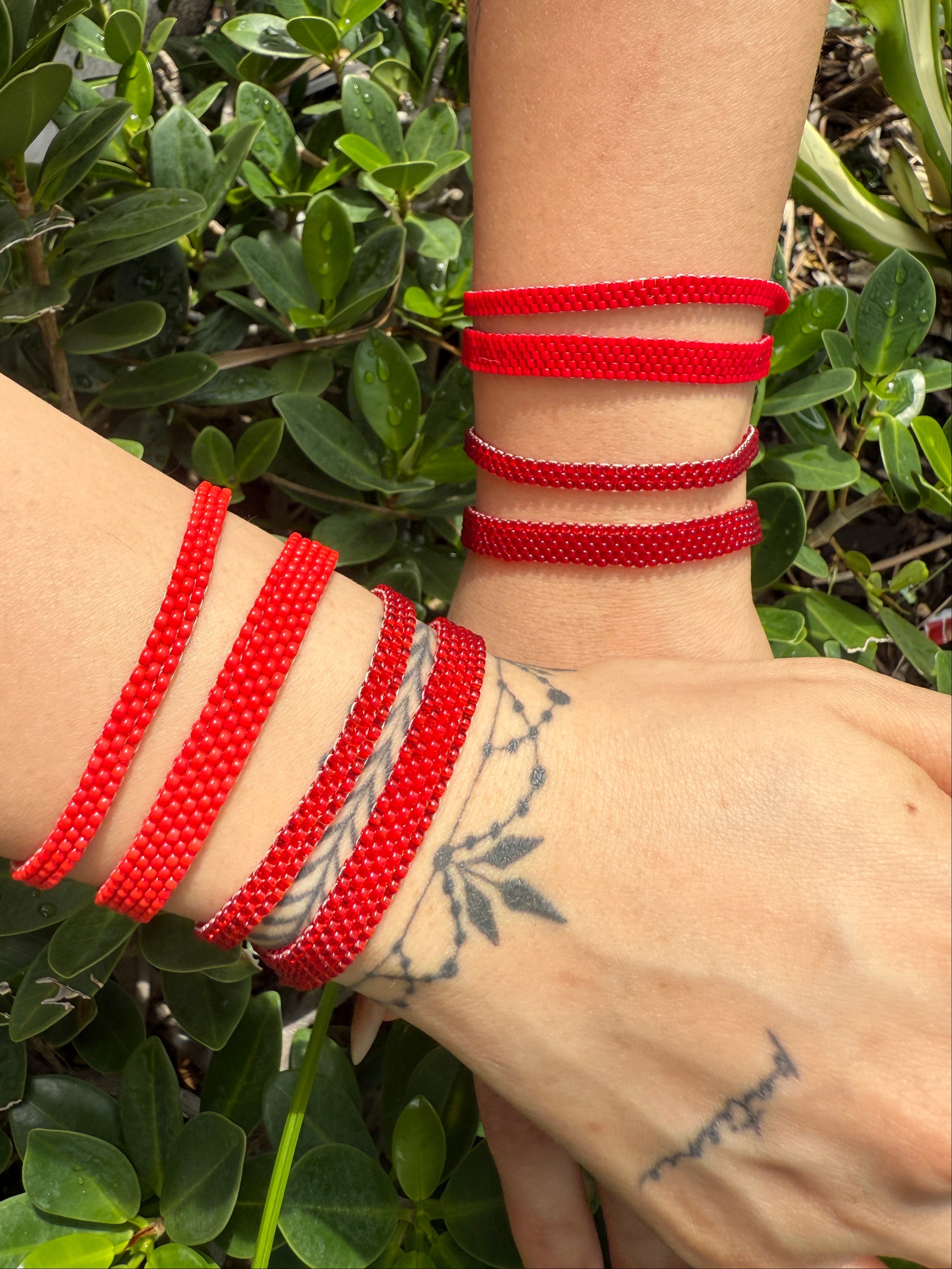 Close-up of a wrist wearing multiple red bracelets with a green leafy background