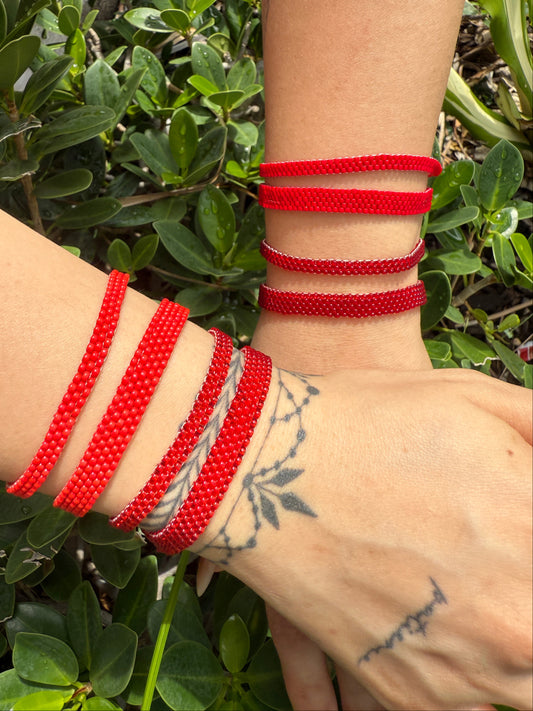 Close-up of a wrist wearing multiple red bracelets with a green leafy background