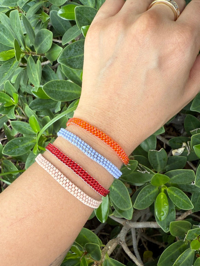Hand wearing multiple colorful beaded bracelets against a green leafy background