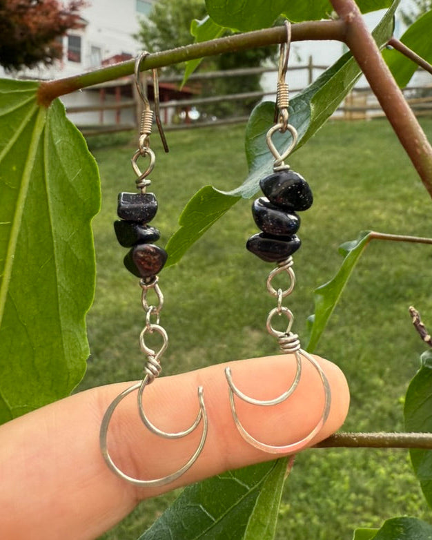 Silver hoop earrings with black beads held against a green leafy background