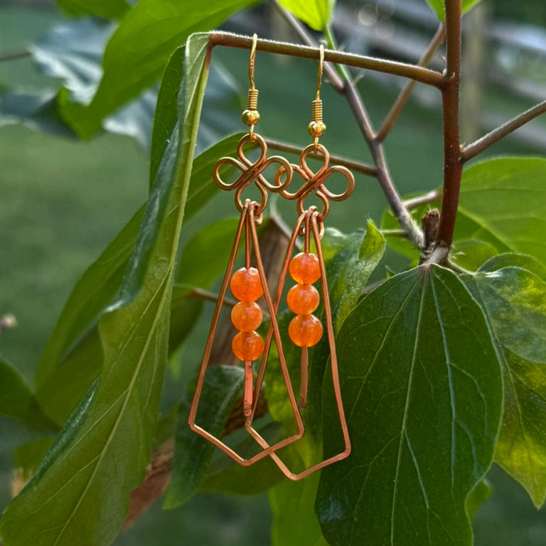 Orange beaded earrings hanging on a branch with green leaves