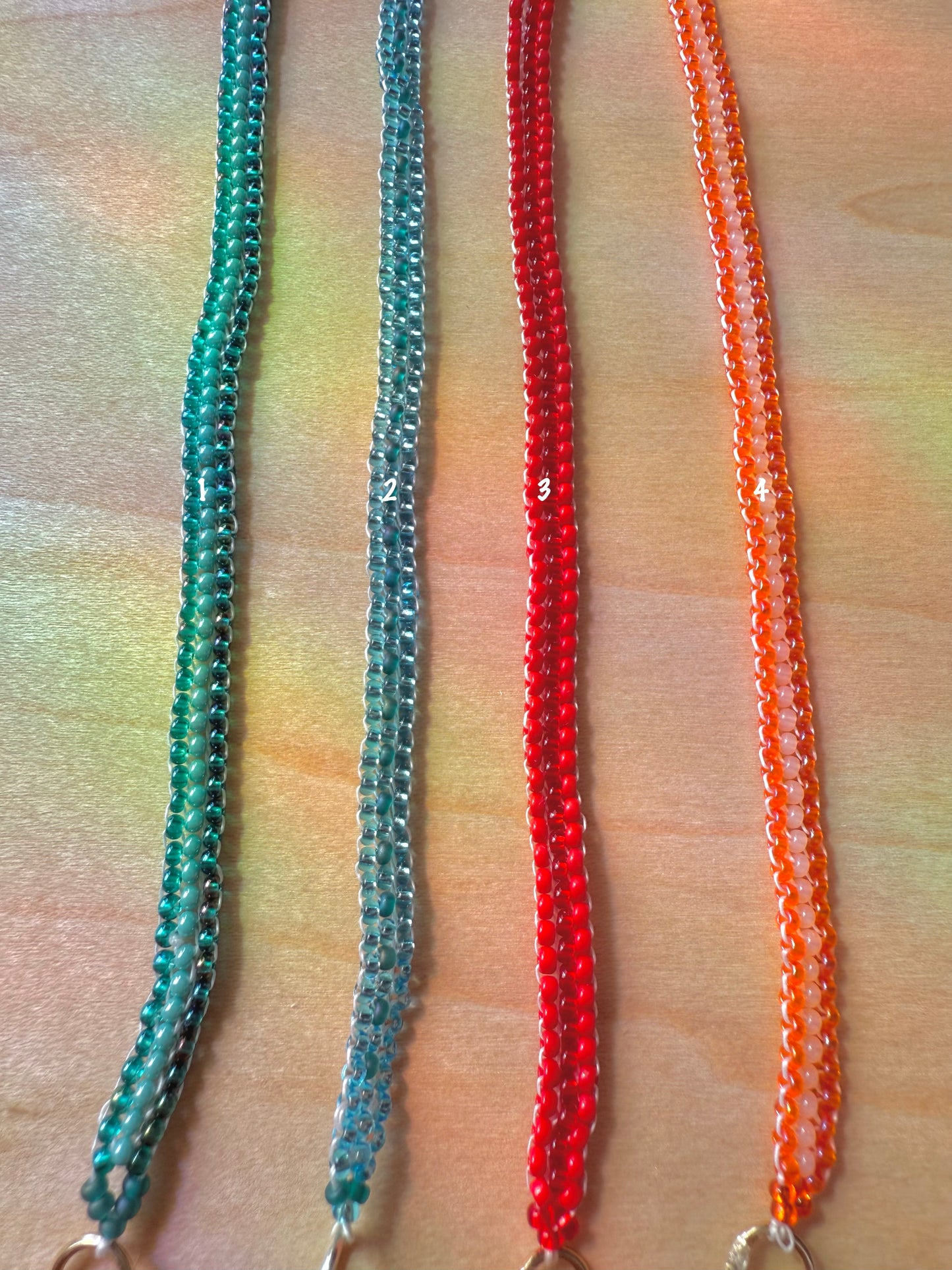 Two beaded necklaces in green and orange on a wooden surface