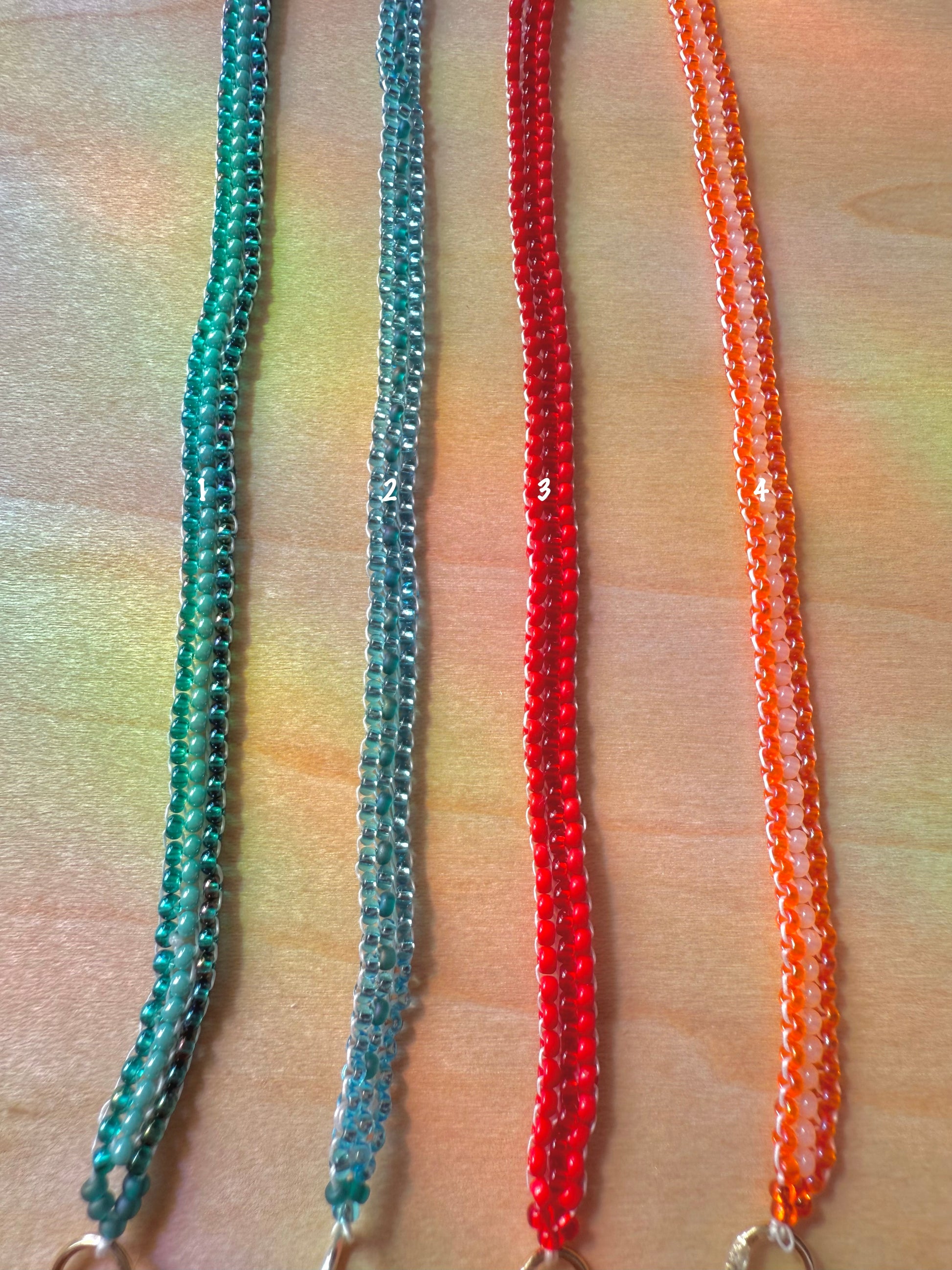 Two beaded necklaces in green and orange on a wooden surface