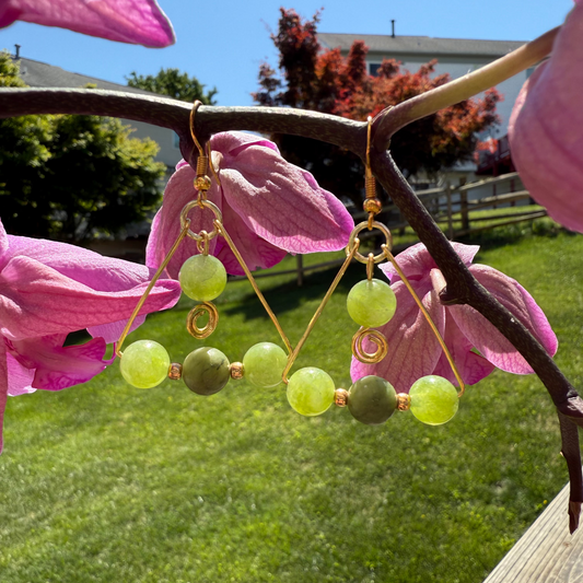 Green beaded earrings hanging on pink flowers with a garden background