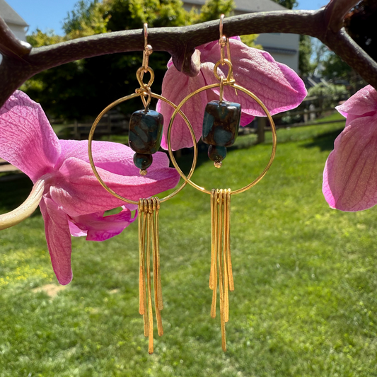 Gold hoop earrings with green beads hanging from pink flowers outdoors.