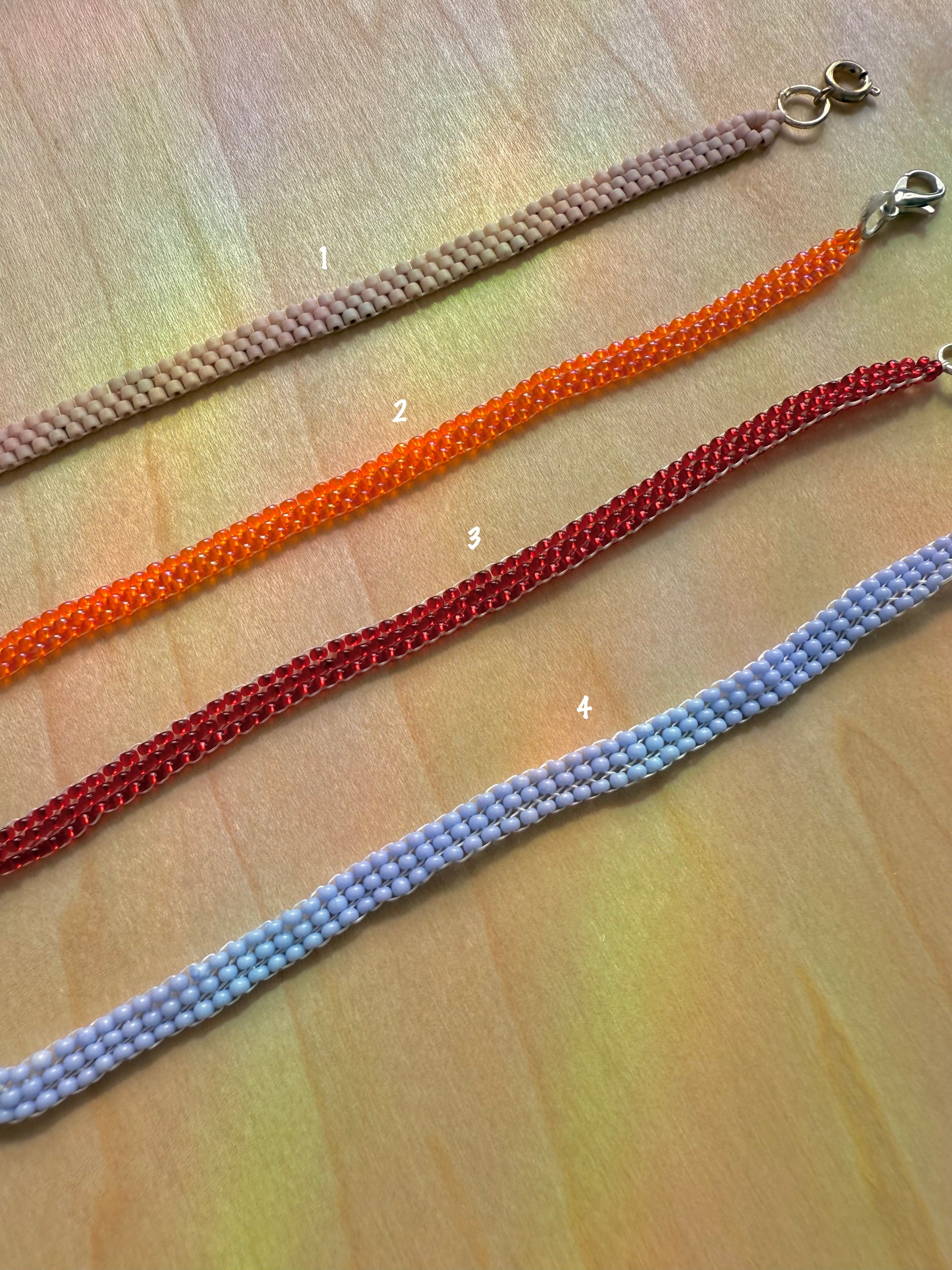Four colorful beaded necklaces on a wooden surface