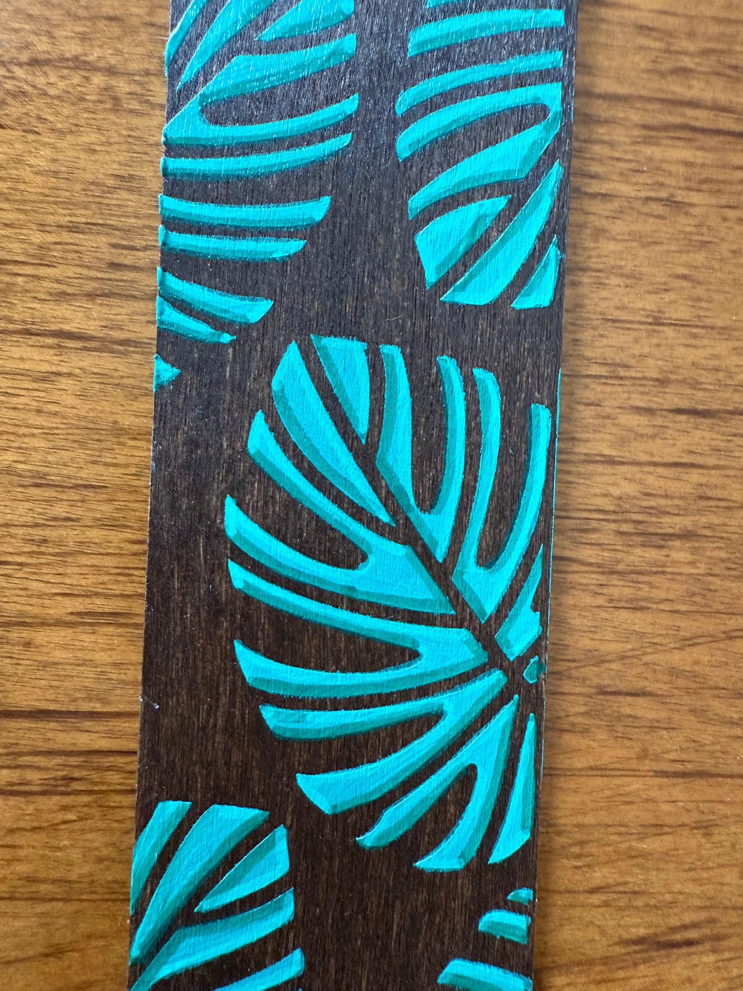 Wooden bookmark with blue leaf pattern on a wooden surface