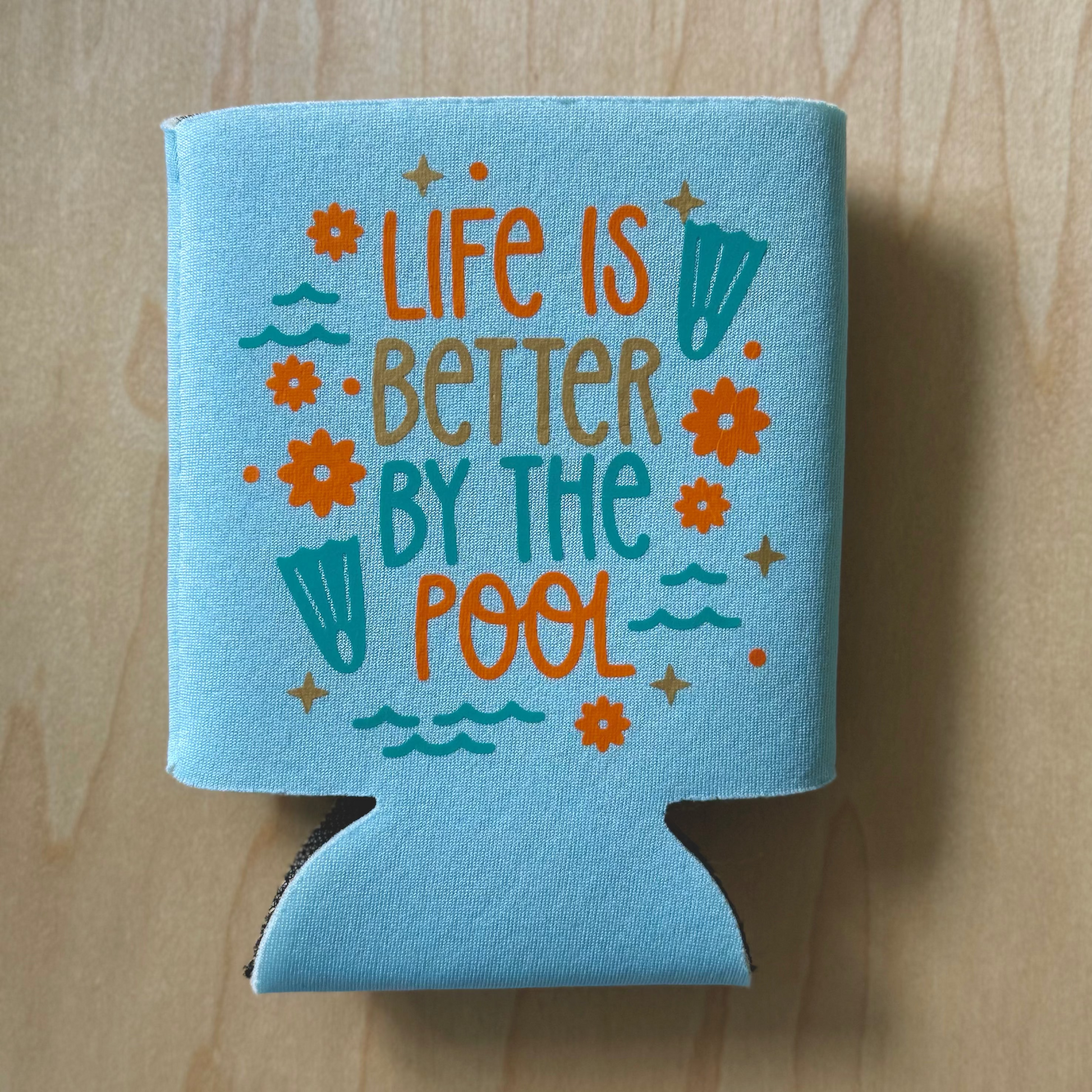Blue can cooler with 'Life is Better by the Pool' text on a wooden surface